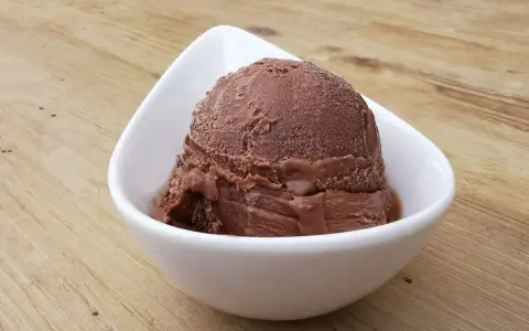 Cremoso helado de platano y chocolate en un cuenco blanco sobre una mesa de madera.