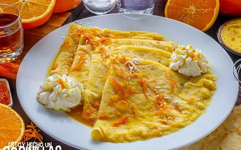 Crepes Suzette, cubiertos con ralladura de naranja y servidos con crema batida.