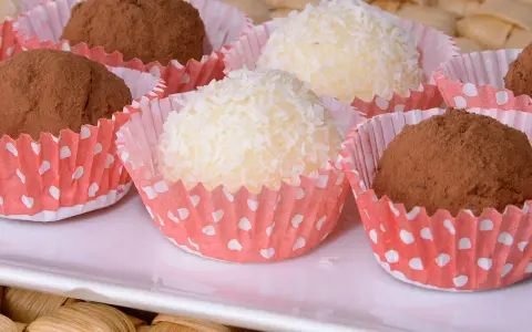 Deliciosas trufas de coco y chocolate, algunas cubiertas de coco rallado y otras de cacao en polvo, presentadas en capacillos rojos con puntos blancos.