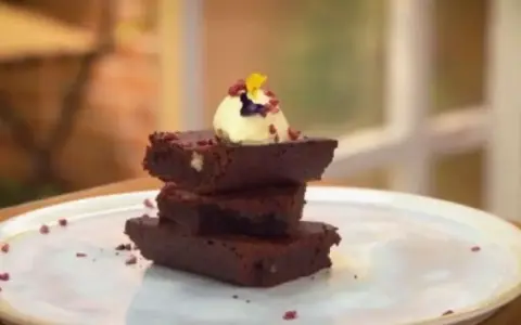 Delicioso brownie airfryer apilado, coronado con helado y pétalos.