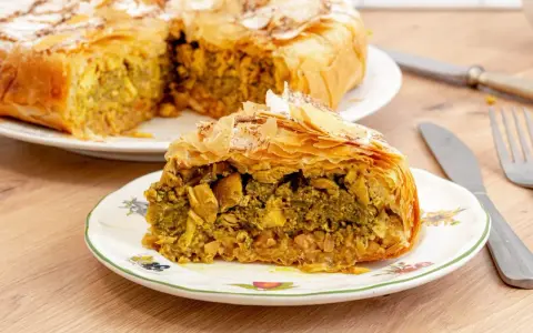Pastela marroqui, un pastel salado de hojaldre relleno de pollo y especias, servido en un plato decorado.