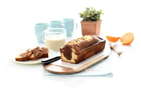 Un delicioso bizcocho marmolado, recién horneado, listo para disfrutar con un vaso de leche y unas rodajas de naranja.