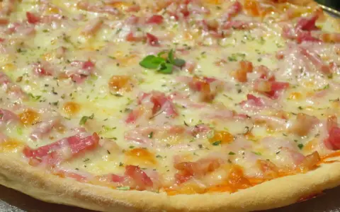 Pizza con masa hecha en Thermomix, cubierta de queso fundido, trocitos de bacon y hierbas aromáticas.