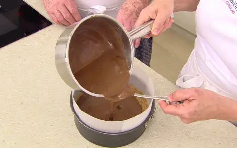 Vertiendo cobertura de chocolate sobre una base de galleta para un delicioso pastel de chocolate.