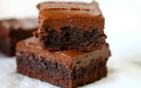 Dos deliciosos brownies con nueces apilados, cubiertos con glaseado de chocolate cremoso.