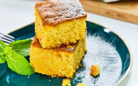 Dos porciones de bizcocho de calabaza, espolvoreadas con azúcar glas, junto a hojas de menta fresca en un plato azul.