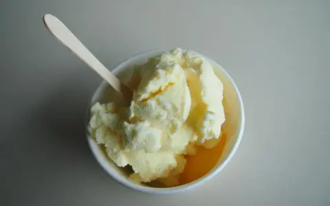Un cremoso helado de melón en un cuenco blanco, listo para ser disfrutado con su cuchara de madera.