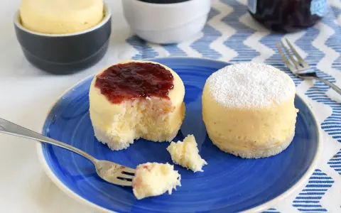 Dos bizcochos de microondas en un plato azul. Uno tiene mermelada de fresa y el otro azúcar glas.