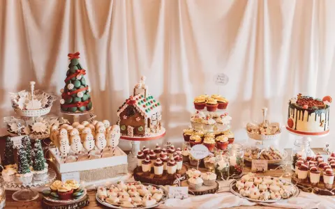 Mesa llena de postres navideños: árbol de macarons, casa de jengibre, muñecos de nieve, cupcakes y galletas.