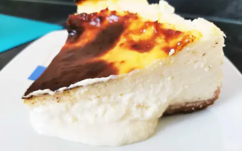 Porción de chese cake con borde quemado y relleno cremoso, servida en plato blanco.
