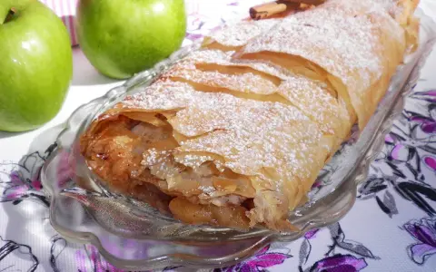 Delicioso strudel de manzana recién horneado, espolvoreado con azúcar glas y acompañado de manzanas verdes frescas y canela.