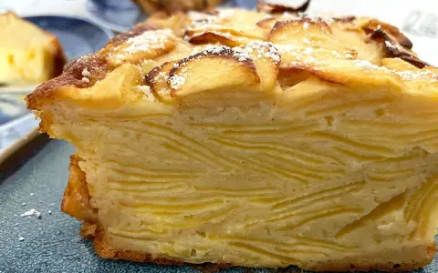 Un trozo de pastel de capas con trozos de manzana en la parte superior, espolvoreado con azúcar glas. Un postre invisible aux pommes.