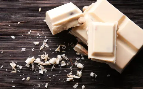 Deliciosos postres con chocolate blanco, trozos y virutas esparcidos sobre una tabla de madera oscura.
