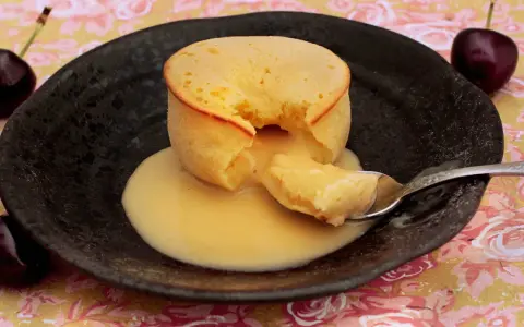 Coulant de chocolate blanco con interior cremoso, servido en plato negro con cerezas.