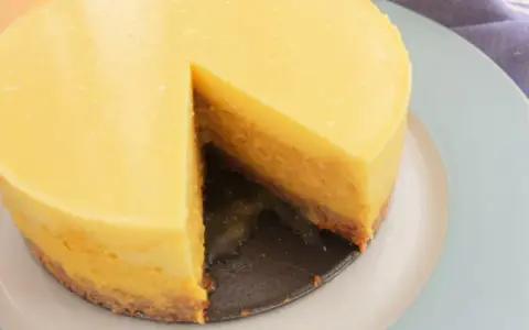 Tarta mango cremosa, con una porción retirada, sobre plato azul claro.