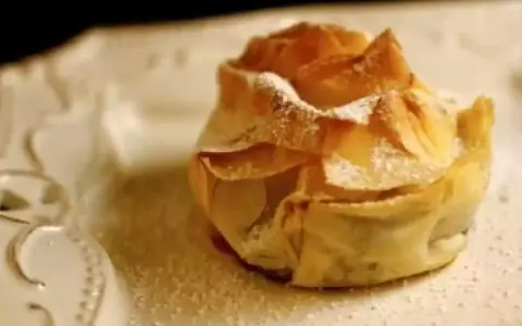 Delicioso saquito de pasta filo relleno de queso, espolvoreado con azúcar glas sobre un plato blanco.