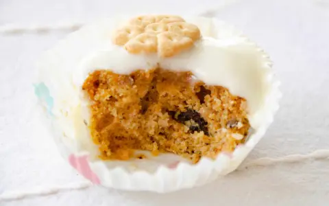 Un muffin de zanahoria con glaseado blanco y una galleta decorativa en forma de flor.