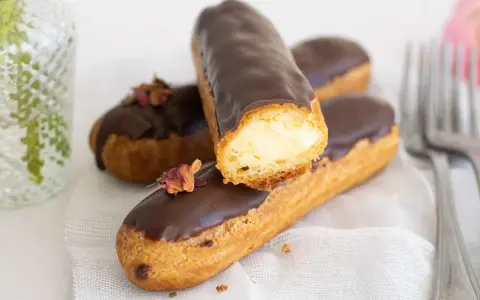 Pastel eclair cubierto de chocolate, relleno de crema. Decorado con pétalos secos.