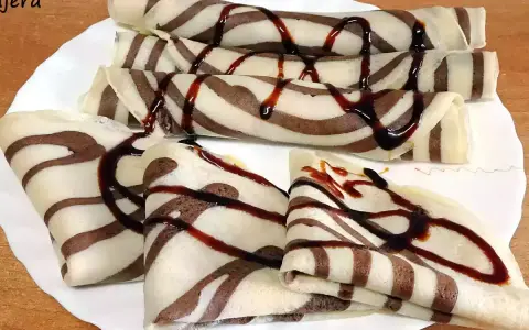 Deliciosos crepes de chocolate rayados, enrollados y doblados, cubiertos con sirope de chocolate.