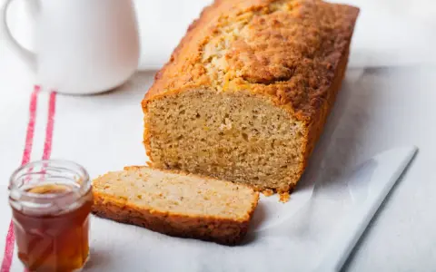 Un delicioso bizcocho con harina integral, recién horneado, con una rebanada cortada y un tarro de miel al lado.