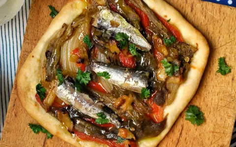 Coca de recapte con verduras asadas y sardinas, decorada con perejil fresco.