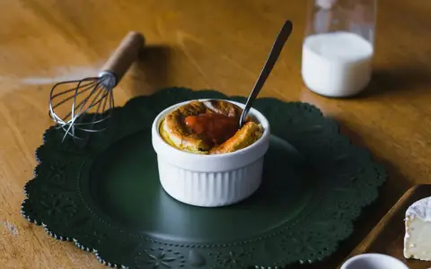 Un esponjoso soufflé con salsa de tomate, listo para disfrutar. Al lado, un batidor y un vaso de leche, ingredientes clave para crear que es un soufflé.