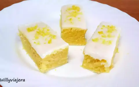 Tres porciones de brownie de limón con glaseado blanco y ralladura de limón, servidas en un plato blanco.