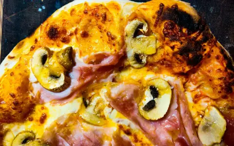 Pizza masa madre con champiñones y jamón, con bordes dorados y burbujas de queso fundido.