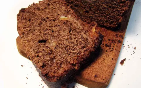 Rebanadas de pan de chocolate húmedo y denso, con trozos de fruta confitada, servidas en una tabla de madera.