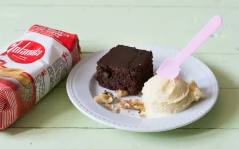 Un delicioso brownie sin huevo con helado de vainilla y nueces, junto a un paquete de Yolanda.