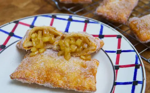 Empanada de manzana recién hecha, dorada y espolvoreada con azúcar. Una está partida, mostrando el relleno jugoso de manzana.