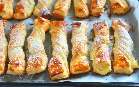 Deliciosos lazos de hojaldre dorados y espolvoreados con azúcar glas, listos para disfrutar.
