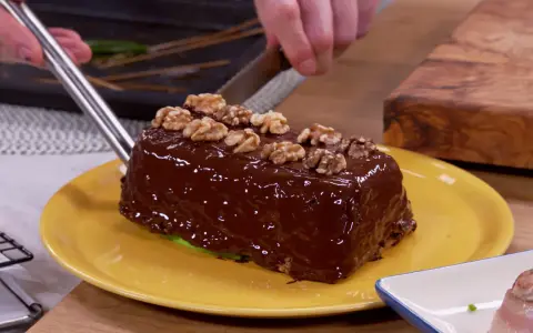 Un delicioso bizcocho de plátano cubierto de chocolate brillante y nueces, listo para ser cortado.