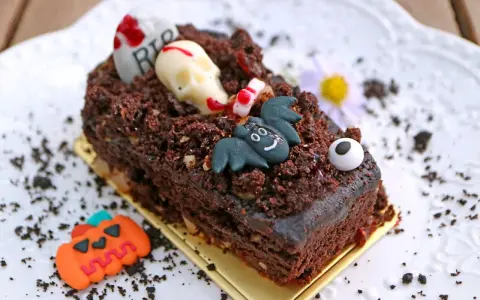 Tartas de Halloween originales: un pastel de chocolate cubierto de tierra de galleta, con un cráneo, un murciélago y una lápida.