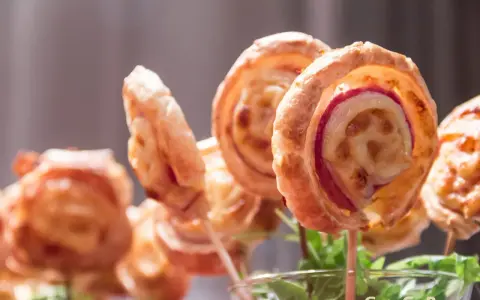 Deliciosas piruletas de hojaldre rellenas de queso y jamón, presentadas en un vaso con hojas verdes.