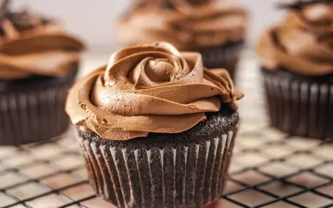Deliciosas magdalenas sin huevo con glaseado de chocolate cremoso, decoradas como una rosa.