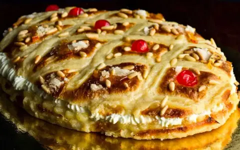 Deliciosa coca de Sant Joan rellena de crema, decorada con piñones, cerezas rojas y azúcar.
