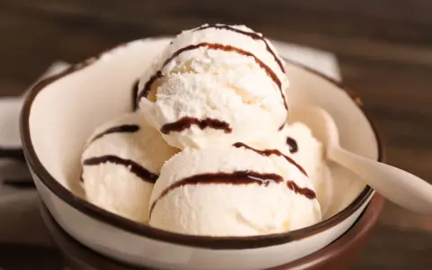 Cuatro bolas de helado de chocolate blanco con sirope de chocolate en un cuenco.