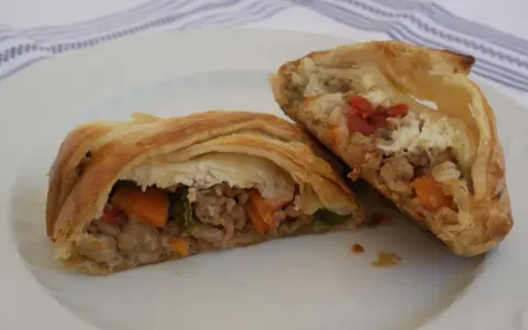 Hojaldre con carne picada y verduras, cortado por la mitad, mostrando el relleno jugoso.