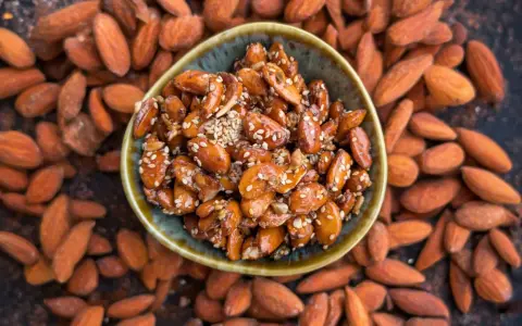 Un cuenco lleno de almendras caramelizadas, cubiertas de semillas de sésamo, rodeadas de almendras enteras.