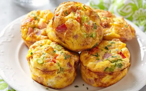 Montón de muffins saludables con huevo, pimiento rojo, cebolleta y jamón, espolvoreados con perejil.