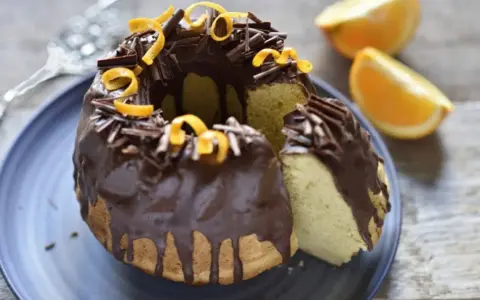 Bizcocho de chocolate y naranja, cubierto con glaseado de chocolate, virutas de chocolate y cáscara de naranja.