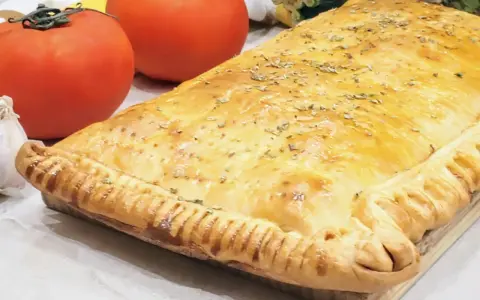 Empanada de pisto dorada y crujiente, con tomates frescos y ajo al lado. ¡Un manjar casero!