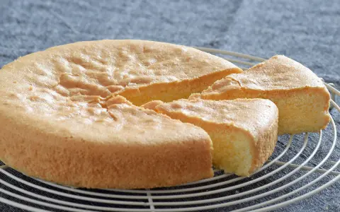Un esponjoso bizcocho sin gluten, recién horneado y cortado en porciones, descansa sobre una rejilla.