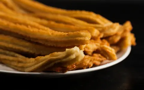 Montón de churros de patata dorados y crujientes apilados en un plato blanco.