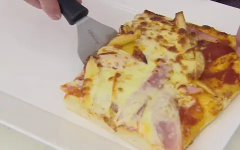 Una rebanada de pan pizza con papas fritas y jamón, lista para ser servida.
