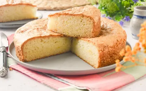 Bizcocho sin huevo esponjoso y dorado, cortado en porciones sobre un plato gris. Ideal para desayunos o meriendas.