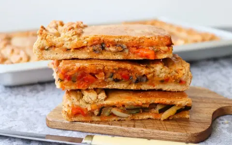 Tres porciones de empanada de verduras apiladas, mostrando el relleno de pimientos, calabacín y tomate.