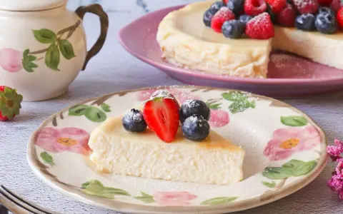 Deliciosa tarta de requesón, decorada con fresas y arándanos, servida en un plato floral.