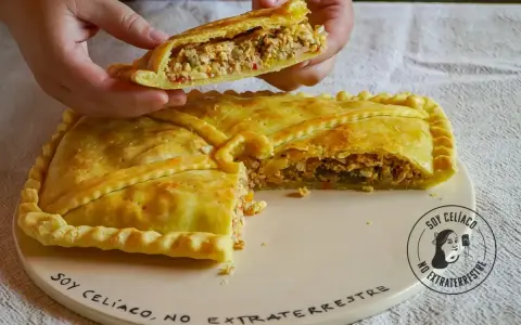 Una mano levanta un trozo de empanada de carne dorada y rellena. La masa crujiente envuelve un sabroso guiso.